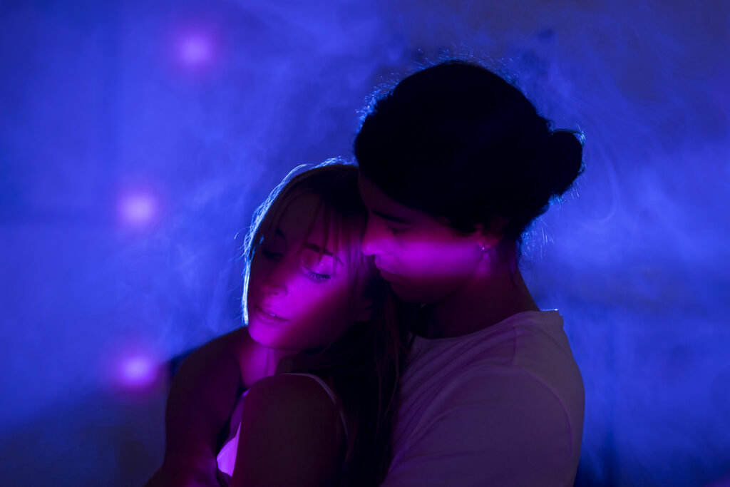Una parella jove que està entre la penombra s'abracen i estan il·luminats per una llum violeta